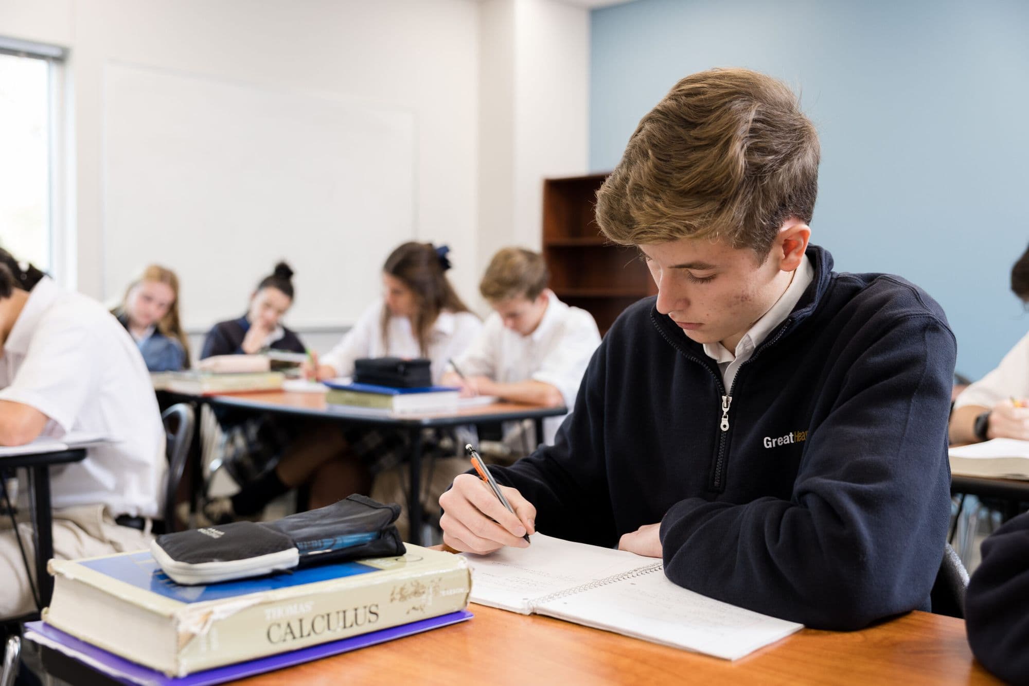 A Great Hearts Northern Oaks student writing alongside classmates, calculus textbook on the desk